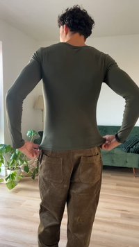 Fekete bőrhatású, hosszú ujjú, olajzöld felső, barna kordbársony nadrággal, melyen nagy zsebek találhatóak. Az anyag simának és rugalmasnak tűnik.