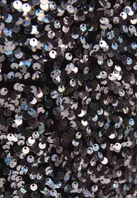 Svart tyg täckt med glänsande, runda paljetter som reflekterar ljus. Paljetterna varierar i färg och skapar en iriserande effekt.