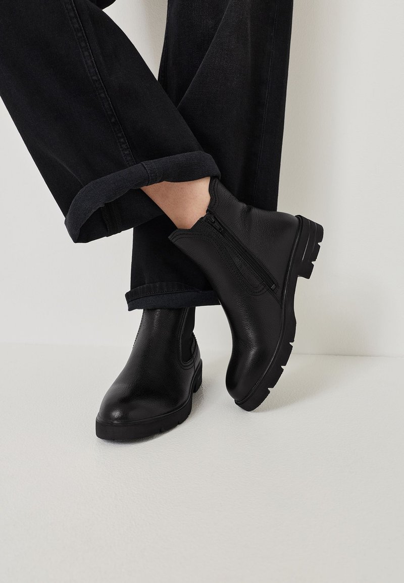 Černé kožené kotníkové boty se zipem na boku, s robustní podrážkou a texturovaným povrchem, spárované s ohrnutými černými džínovými kalhotami.