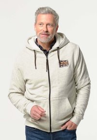Lichtgrijze zip-up hoodie met een voorkantzak, trekkoordcapuchon en Brits vlagembleem. De stof lijkt zacht, met een gladde textuur.