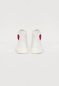 Sneakers bianchi alta con una texture liscia, caratterizzati da un cuore ricamato rosso sul retro. Suola in gomma, design minimalista.