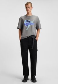 Gray short-sleeve T-shirt featuring a blue and white graphic print. Paired with black cargo pants and black sneakers with a textured finish.