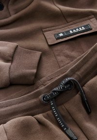 Brun bomulds sweatshirtsæt og joggersæt med en tekstureret lomme, snøre med trykt branding og ribbede manchetter.