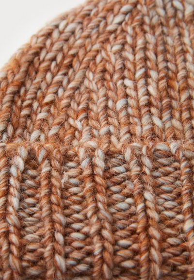 Gebreide muts in oranje en crèmekleuren. Kenmerkt zich door dik, gestructureerd garen met een dichte, geribbelde structuur. Zacht en warm materiaal.