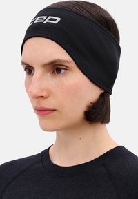 Zwart atletisch hoofdbandje gemaakt van textuurstof, met een prominent wit logo. Zit strak rond het voorhoofd.