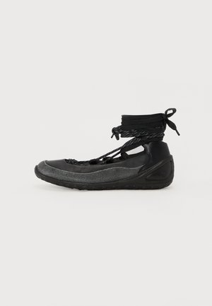Black footwear featuring a low profile, textured upper, and a flexible sole; secured with a lacing system and ankle wrap for fit.