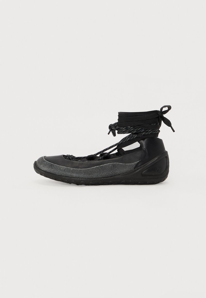 Chaussures noires avec un profil bas, un dessus texturé et une semelle flexible ; maintenues par un système de laçage et un enroulement de cheville pour un ajustement parfait.