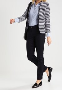 Navy and white striped blazer over a light blue button-up shirt, paired with black slim-fit trousers and shiny black loafers.