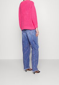Rosa Strickpullover, lässige Passform; kombiniert mit blauen Jeanshosen mit gewölbten Nähten und fransigen Säumen; schwarze Absatzsandalen.
