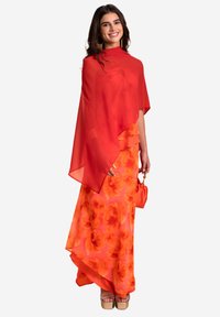 Roter, transparenter, asymmetrischer Umhang über einem lebhaft orangefarbenen Blumen-Maxikleid. Der Look wird mit Plateau-Sandalen und einer kleinen Handtasche abgerundet.