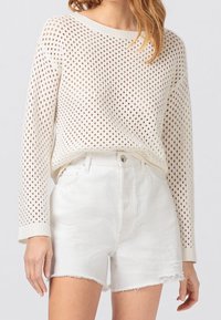 Biały dzianinowy sweter z otwartym wzorem siateczki i długimi rękawami, zestawiony z białymi denimowymi szortami z wysokim stanem i postrzępionymi brzegami.