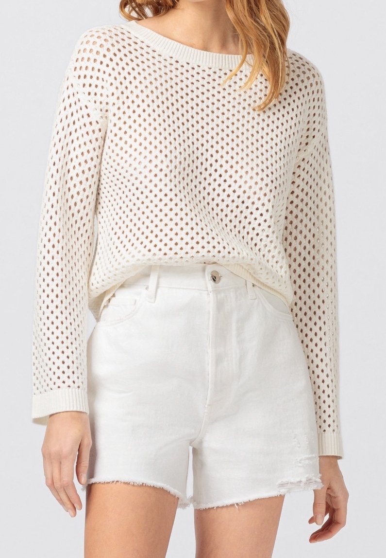 Biały dzianinowy sweter z otwartym wzorem siateczki i długimi rękawami, zestawiony z białymi denimowymi szortami z wysokim stanem i postrzępionymi brzegami.