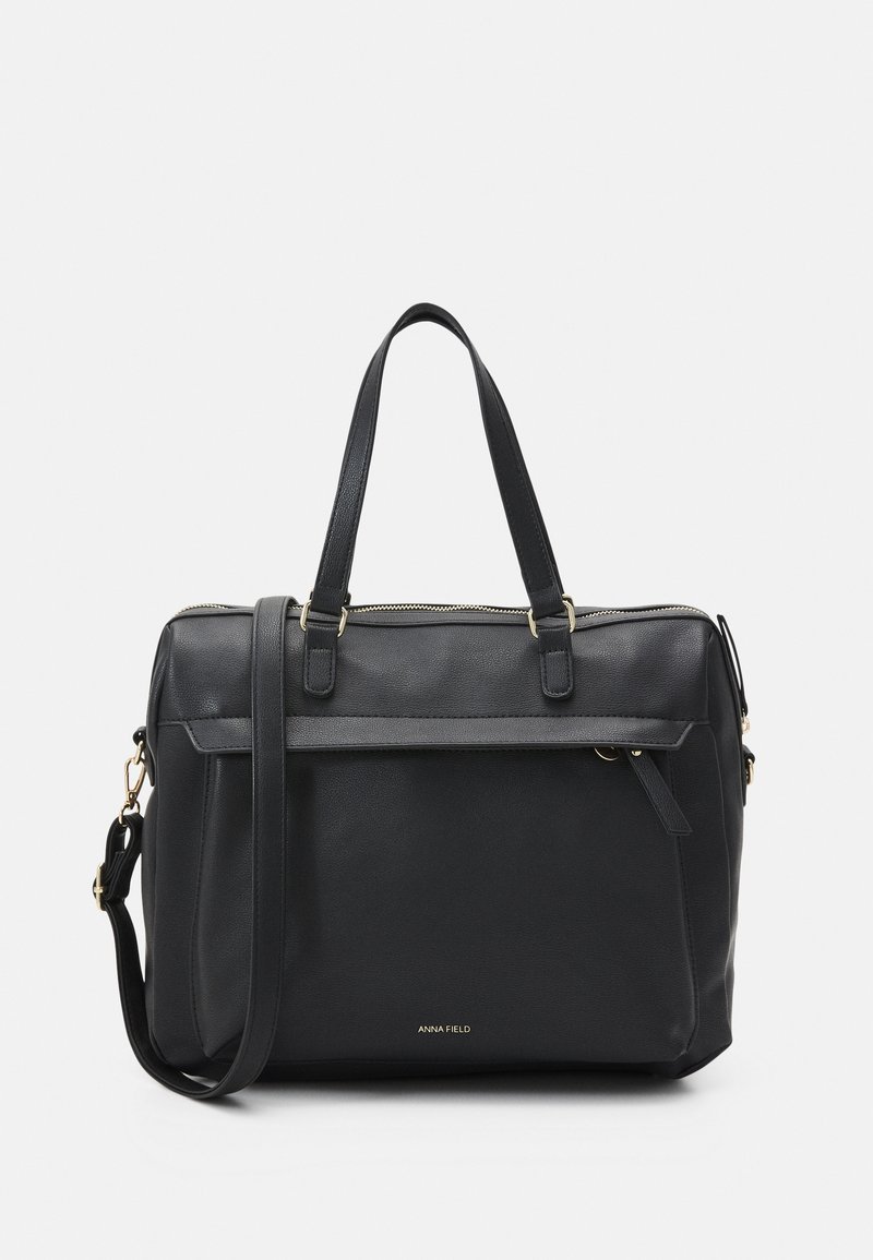 Sac cabas en cuir noir avec doubles poignées, bandoulière détachable, poche zippée à l'avant et logo doré "Anna Field" sur le devant.