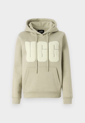 Gaiša olīvu zaļa kapuce ar lielu, teksturētu UGG logo krēmkrāsā. Tai ir kapuce ar aukliņu un priekšējais kabatas maisiņš.