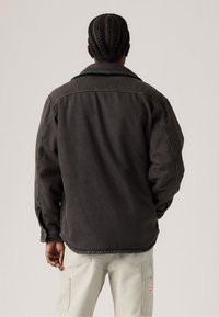 Mørk denimjakke med grøn krave, løs pasform og synlige syninger. Bæres med lyse cargo-bukser.