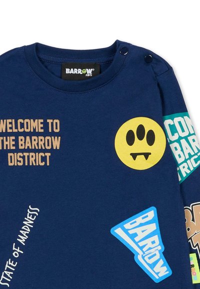 T-shirt per bambini di colore blu navy con vari grafica colorate, inclusi testi e una faccina sorridente gialla con tre occhi, e bottoni a pressione sulla spalla.