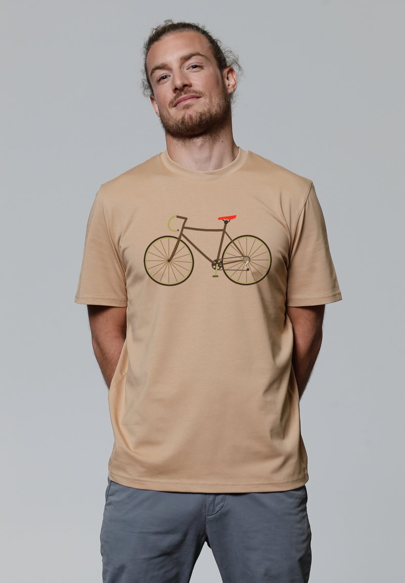Beige t-shirt van zacht materiaal met een grafisch ontwerp van een fiets in bruin met groene en oranje accenten. Korte mouwen, relaxte pasvorm.
