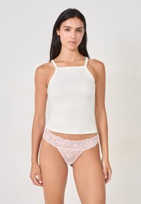 Débardeur blanc à côtes avec des bretelles spaghetti, associé à un string en dentelle florale rose. Le tissu a une texture lisse et une silhouette ajustée.