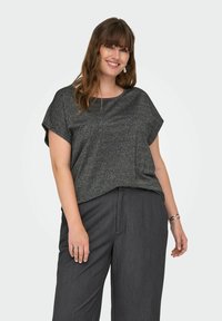 Top noir à manches courtes avec une finition texturée et scintillante. Associé à un pantalon large gris foncé. Présente un col rond et une coupe ample.