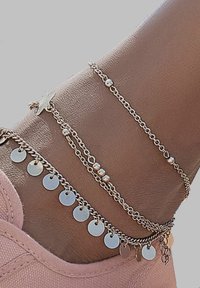 Gold-tone ankle bracelets with varying chain designs. Includes round charms and beads, featuring a star accent. Displayed on a foot.