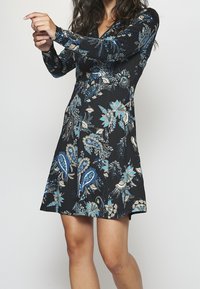 Langärmliges schwarzes Kleid mit einem blauen und beigen Blumen-Paisley-Muster, V-Ausschnitt und einer A-Linie mit einem schwingenden Rock.