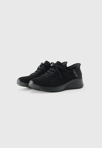 Pair of black knitted low-top sneakers with lace-up design and textured soles on a plain white background.