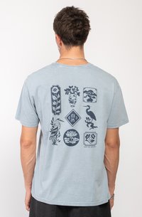 Camiseta de algodón de color azul claro con estampados gráficos oscuros de flores, pájaros y formas decorativas en la parte posterior. Mangas cortas y cuello redondo.