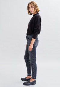 Maglione nero, jeans grigi aderenti e mocassini neri. Tessuto liscio, design semplice, con jeans alla caviglia e accenti di calzature minimaliste.