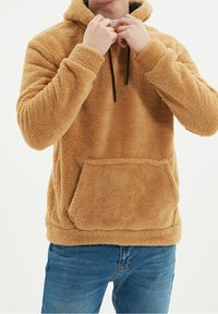 Beżowa bluza z kapturem wykonana z polaru, z przednią kieszenią, regulowanym sznurkiem przy kapturze i długimi rękawami. Miękka w dotyku i o luźnym kroju.