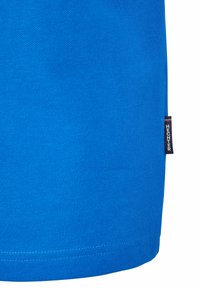 Chemise bleu vif à manches courtes avec une finition en tissu texturé et un ourlet droit. Présente une petite étiquette noire avec des lettres blanches sur le côté.