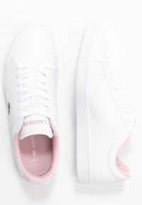 Due coppie di sneakers bianche Lacoste viste dall'alto, con dettagli rosa all'interno della scarpa. Design pulito e minimalista su uno sfondo bianco.