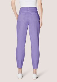 Lavendel katoenmengsel broek met een taps toelopende pasvorm, voorzien van twee achterzakken en ritsen bij de enkels, gecombineerd met witte schoenen.