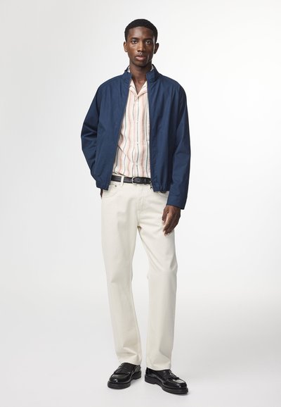 Marineblå letvægtsjakke, stribet skjorte med knapper, cremede bukser, sort bælte og polerede sko. Har en stående krave og slim-fit design.