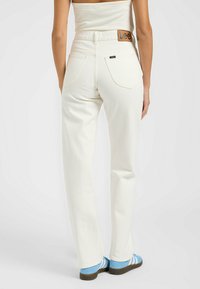 Jeans blancos de cintura alta con pierna recta, que cuentan con un parche de cuero con el logo de Lee en la parte trasera de la cintura y dos bolsillos traseros.