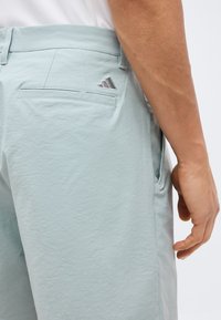 Ανοιχτό μπλε σορτς με πίσω τσέπη welt και μικρό κεντημένο λογότυπο στη μέση, συνδυασμένα με λευκό πουκάμισο.