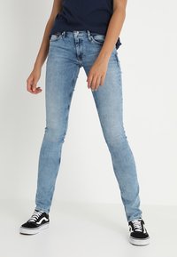 Vaqueros ajustados de un azul claro hechos de denim, con un diseño clásico de cinco bolsillos y un ligero desvanecimiento. Combinados con zapatillas en blanco y negro.