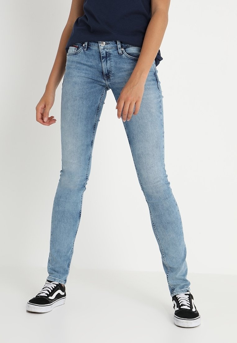 Vaqueros ajustados de un azul claro hechos de denim, con un diseño clásico de cinco bolsillos y un ligero desvanecimiento. Combinados con zapatillas en blanco y negro.