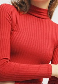 Top a collo alto rosso a coste con maniche lunghe, caratterizzato da un design aderente e un tessuto testurizzato. Nessun dettaglio o motivo visibile.