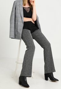 Grå rutig blazer över en svart spets-camisole, i kombination med texturerade grå utsvängda byxor och svarta klackstövlar. Neutral bakgrund.