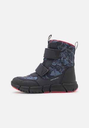 Botte imperméable noire et bleue avec des accents rouges, présentant un design texturé, deux sangles Velcro et une semelle en caoutchouc robuste.