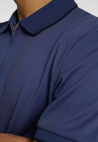 Polo navy en tissu lisse, doté d'un col en tricot texturé et d'une fermeture éclair. Manches courtes avec des accents subtils.