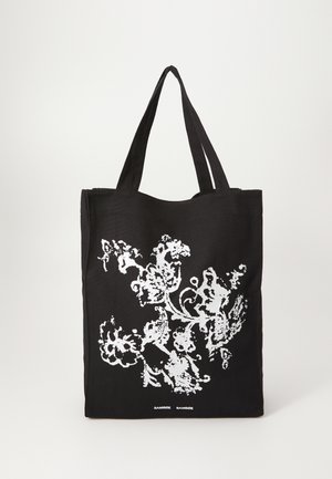 Black tote bag with white floral design. Made of fabric, features two sturdy straps, and has a smooth texture. "Samsøe Samsøe" printed at the bottom.