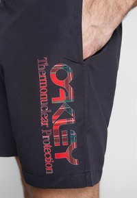 Shorts navy en tissu léger avec un logo "Oakley" et du texte multicolores bien visibles sur le côté, agrémentés d'un accent à carreaux.