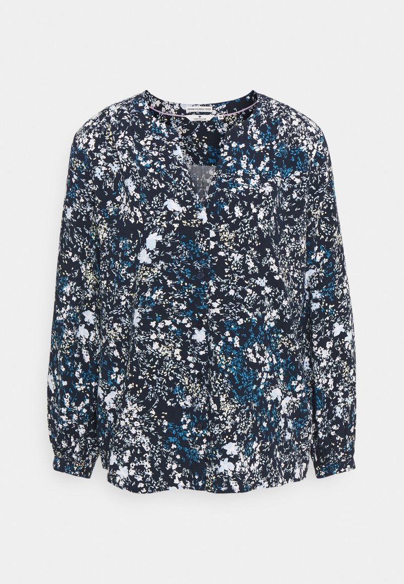 Blouse bleu marine à manches longues avec imprimé floral blanc et bleu, encolure en V et poignets froncés, présentée sur fond blanc.