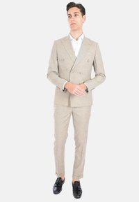 Completo doppiopetto beige chiaro con tessuto testurizzato, taglio aderente, abbinato a una camicia bianca fresca e mocassini neri.