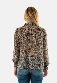 Blusa trasparente con un motivo floreale in tonalità di beige e nero, maniche lunghe e colletto. La vista posteriore mostra due tasche e un orlo arrotondato.