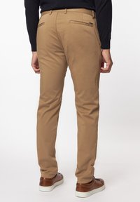 Khaki chino's van een katoenmengsel, slim fit met achterzakken en ritsen, gecombineerd met bruine sneakers en een zwarte trui.