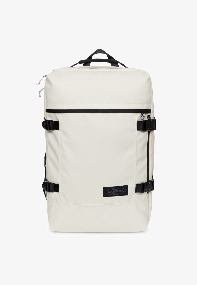 Kremowy plecak o gładkiej fakturze, czarne paski, klamry i naszywka z logo. Posiada prostokątny kształt oraz wiele przegródek.
