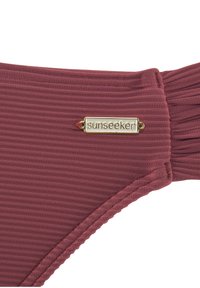 Bordeauxfarbene, gerippte Bikinihose mit goldener "Sunseeker"-Logo-Plakette und gerafftem seitlichem Detail. Die Textur wirkt weich und dehnbar für Komfort.