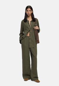 Oliwkowa, długorękawowa koszula zapinana na guziki z luźnymi spodniami. Strój wykonany jest z fakturowanej tkaniny, uzupełniony naszyjnikiem i torebką.